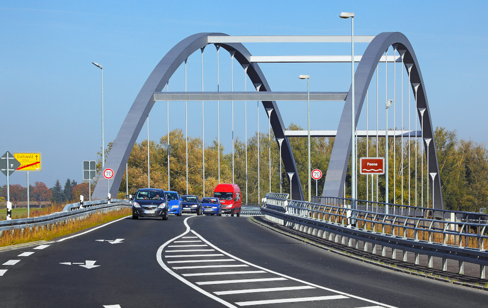 Autos kommen von einer Brücke gefahren, die von zwei großen Metallbögen und mehreren Metallstreben getragen wird.