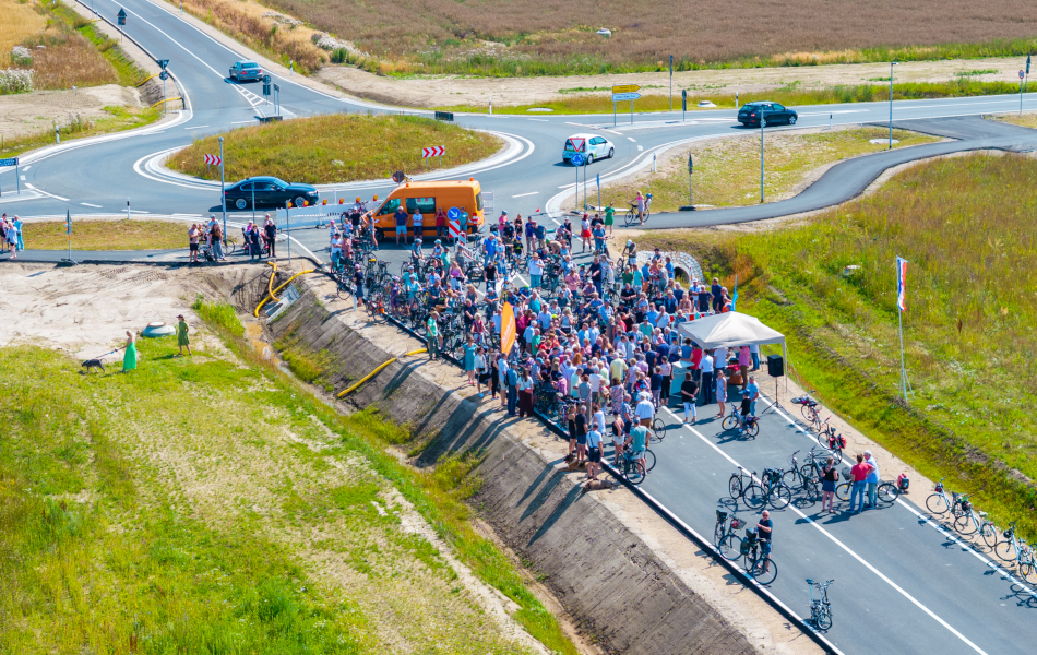 Viele Menschen stehen auf einer neuen Straße. Sie feiern die Eröffnung. Die Straße führt zu einem neuen Kreisverkehr auf dem Land. © Pixelbox15 Viele Menschen stehen auf einer neuen Straße. Sie feiern die Eröffnung. Die Straße führt zu einem neuen Kreisverkehr auf dem Land.