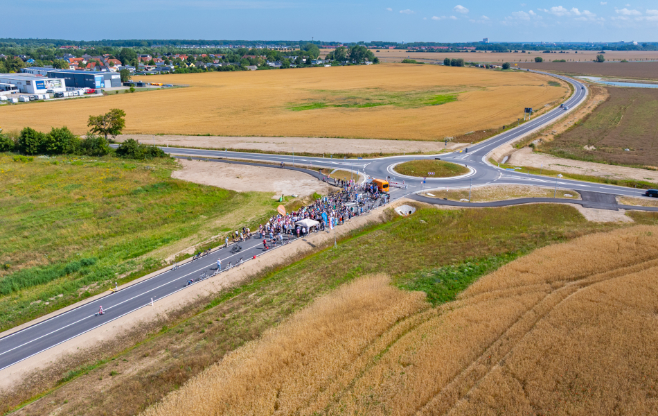 Viele Menschen stehen auf einer neuen Straße. Sie feiern die Eröffnung. Die Straße führt zu einem neuen Kreisverkehr auf dem Land. © Pixelbox15 Viele Menschen stehen auf einer neuen Straße. Sie feiern die Eröffnung. Die Straße führt zu einem neuen Kreisverkehr auf dem Land.
