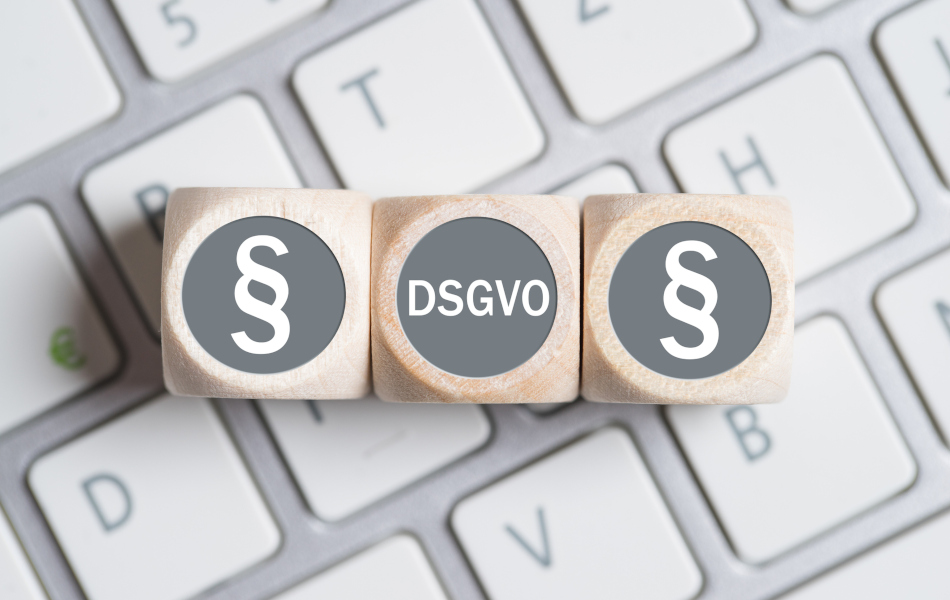 Drei Würfel liegen nebeneinander auf einer Tastatur. Auf den beiden äußeren Würfeln ist jeweils ein Paragraphen-Symbol, auf dem mittleren steht "DSGVO".