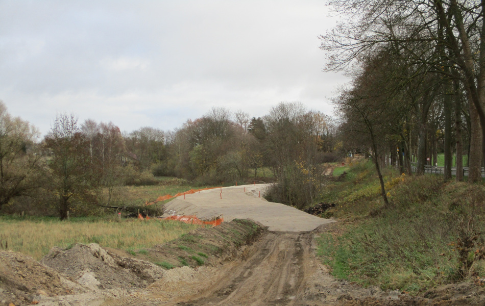 Neben einer Straße ist auf einer Grünfläche ein Sandweg aufgeschüttet.