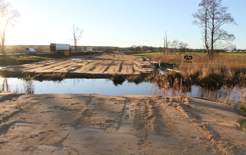 Auf beiden Uferseiten eines Flusses, der Ziese, liegt plattgewalzter Sand. Im Hintergrund verläuft eine viel befahrene Straße.