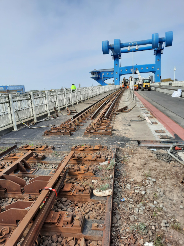 Über eine Brücke führen Gleise, aus denen ein Abschnitt entfernt wurde. Im Hintergrund sind Baumaschinen und ein blauer Brückenaufbau.