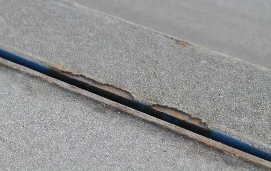 Zwischen zwei Fahrbahnkanten ist ein Spalt, der Abplatzungen und Roststellen aufweist.