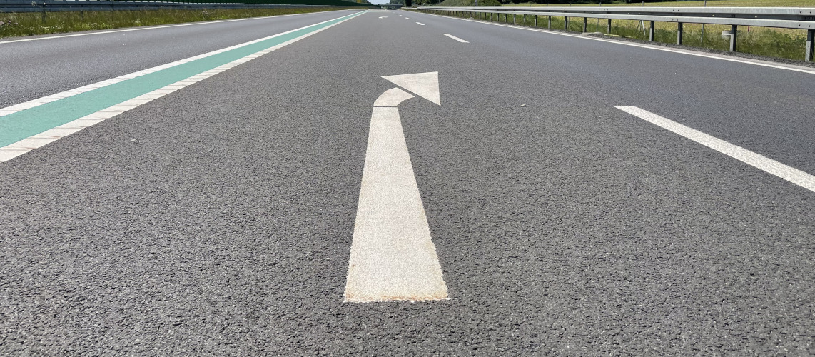 Auf einer mehrspurigen Straße zeigt ein weißer Pfeil auf der Fahrbahn nach rechts.