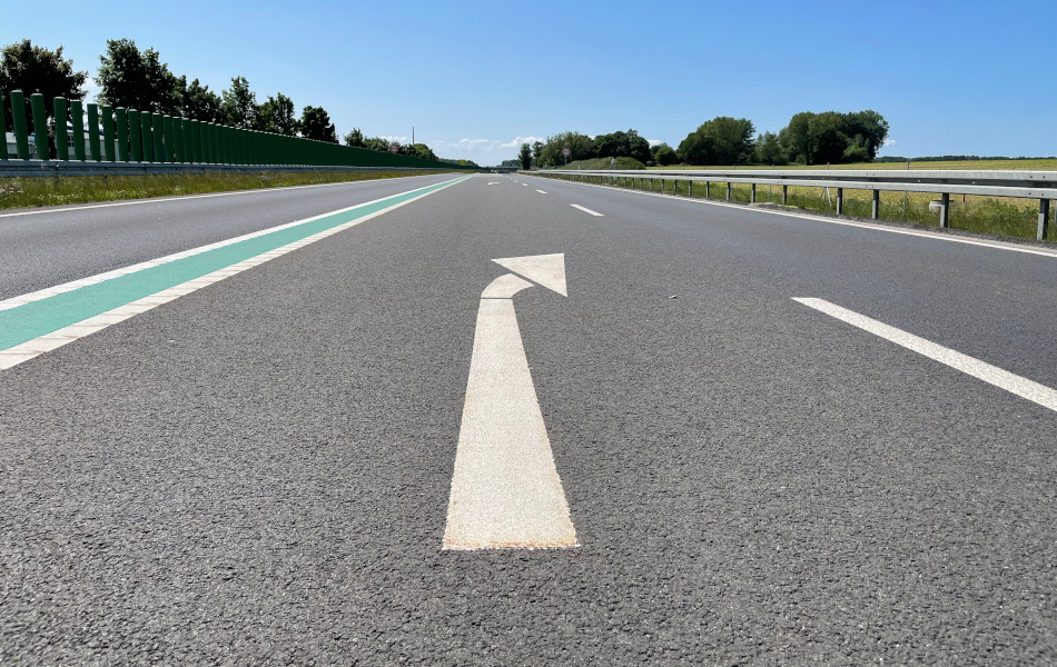 Auf einer mehrspurigen Straße zeigt ein weißer Pfeil auf der Fahrbahn nach rechts.