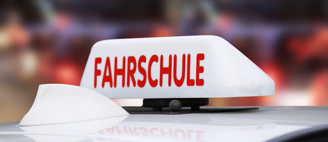 Ein Schild mit der Aufschrift "Fahrschule" ist auf einem Autodach. 