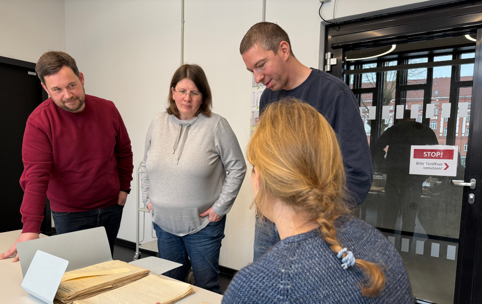 Four people are examining historical files spread out on a table.