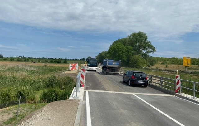 Ein Bus und zwei Autos fahren über eine Brücke aneinander vorbei. Im Hintergrund stehen Bäume.