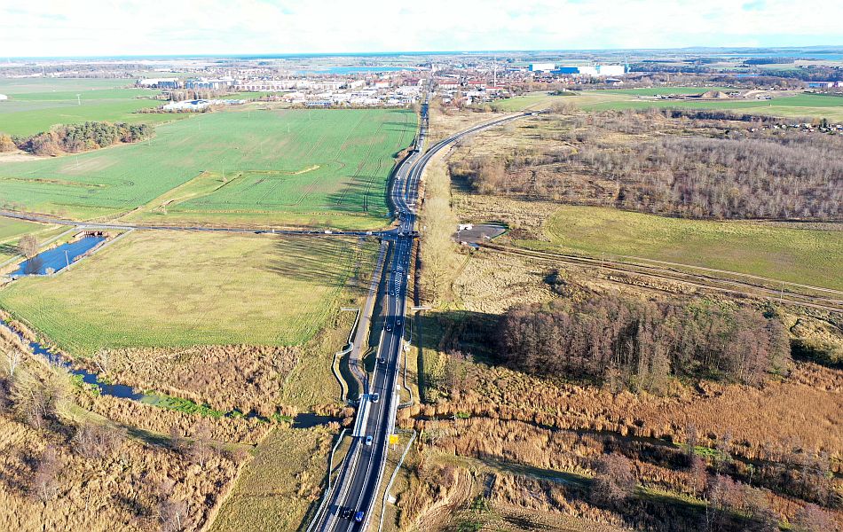 Luftaufnahme einer neuen Straße mit Brücke über die Ziese, Felder und Feuchtgebiete im Vordergrund, die Stadt Wolgast in der Ferne sichtbar.