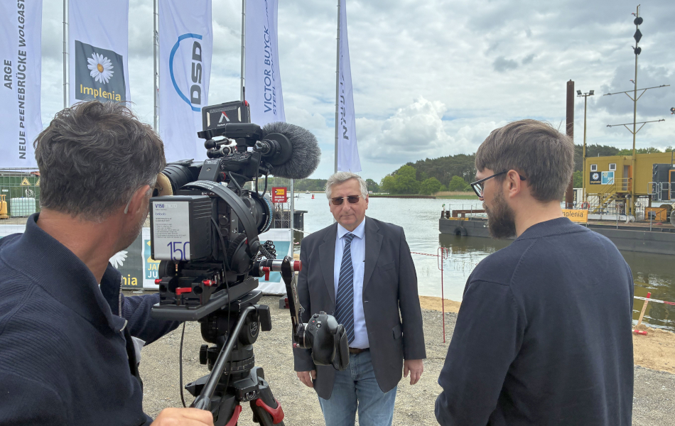 Interview-Situation beim Baustart der Peenestrombrücke mit Kamerateam, Gesprächspartner und Baustellenbereich am Wasser. © strassen-mv.de Interview-Situation beim Baustart der Peenestrombrücke mit Kamerateam, Gesprächspartner und Baustellenbereich am Wasser.