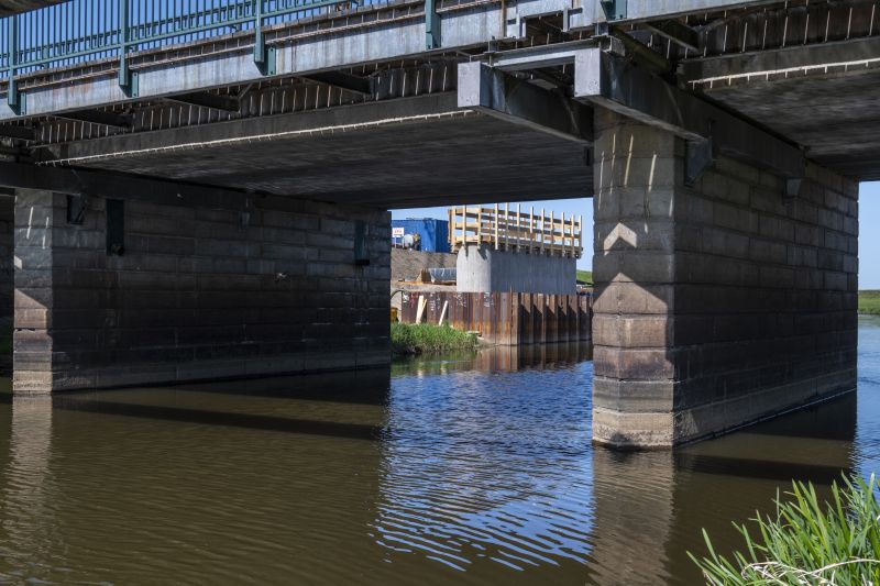 Eine Brücke führt über einen Fluss, zwei Betonpfeiler ragen aus dem Wasser. Dahinter steht ein neugebauter Pfeiler für eine neue Brücke.