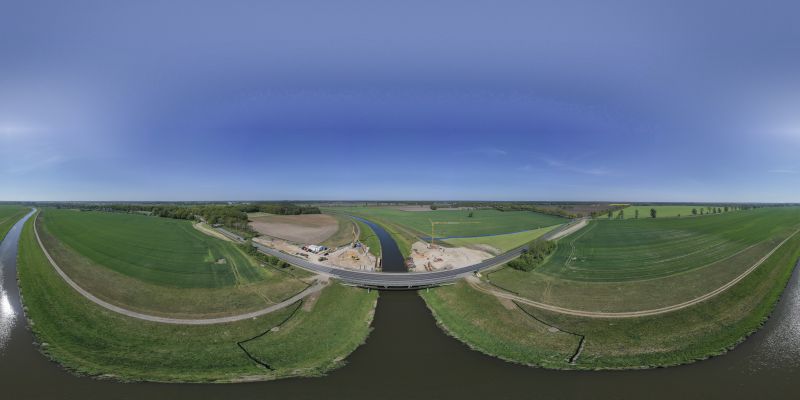 Eine Straßenbrücke führt über einen Fluss und wirkt durch die ungewöhnliche Foto-Perspektive gebogen. Neben der Brücke ist auf beiden Uferseiten eine Baustelle eingerichtet. Rundherum sind viele Felder und der weitere Verlauf des Flusses. © Matthäi-Gruppe Eine Straßenbrücke führt über einen Fluss und wirkt durch die ungewöhnliche Foto-Perspektive gebogen. Neben der Brücke ist auf beiden Uferseiten eine Baustelle eingerichtet. Rundherum sind viele Felder und der weitere Verlauf des Flusses.