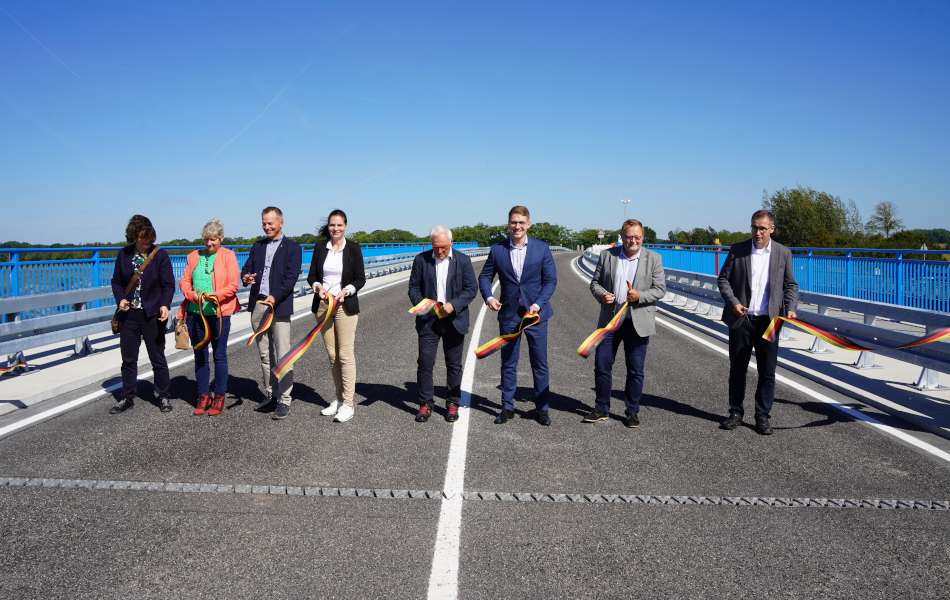Mehrere Menschen stehen in einer Reihe auf der Brücke. Sie haben gerade ein Band zur offiziellen Verkehrsfreigabe durchgeschnitten und halten die Stoffreste in der Hand. © strassen-mv.de Mehrere Menschen stehen in einer Reihe auf der Brücke. Sie haben gerade ein Band zur offiziellen Verkehrsfreigabe durchgeschnitten und halten die Stoffreste in der Hand.
