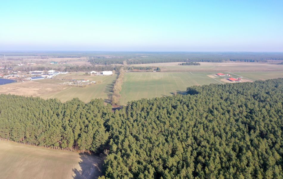 Blick von oben über Wälder und Felder. Am Rand der Felder sind mehrere Gebäude. 