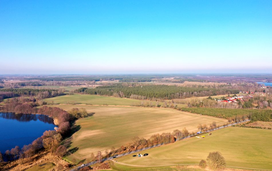Blick von oben über Felder und Wälder. Eine Straße, umsäumt von Alleebäumen, führt durch zwei Felder und zu einer Stadt (Mirow). An einem der Felder befindet sich ein See. 
