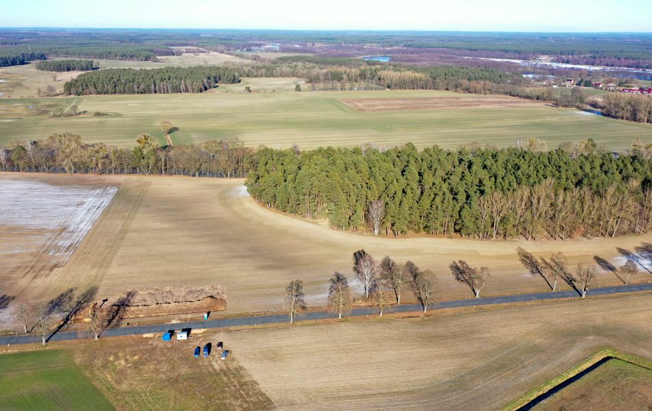 Blick über Felder und Wälder. Eine Straße führt quer durch die Felder. An der Straße ist ein Bagger aktiv und mehrere Fahrzeuge stehen auf einem Feld. Hier beginnen erste vorbereitende Bauarbeiten. 