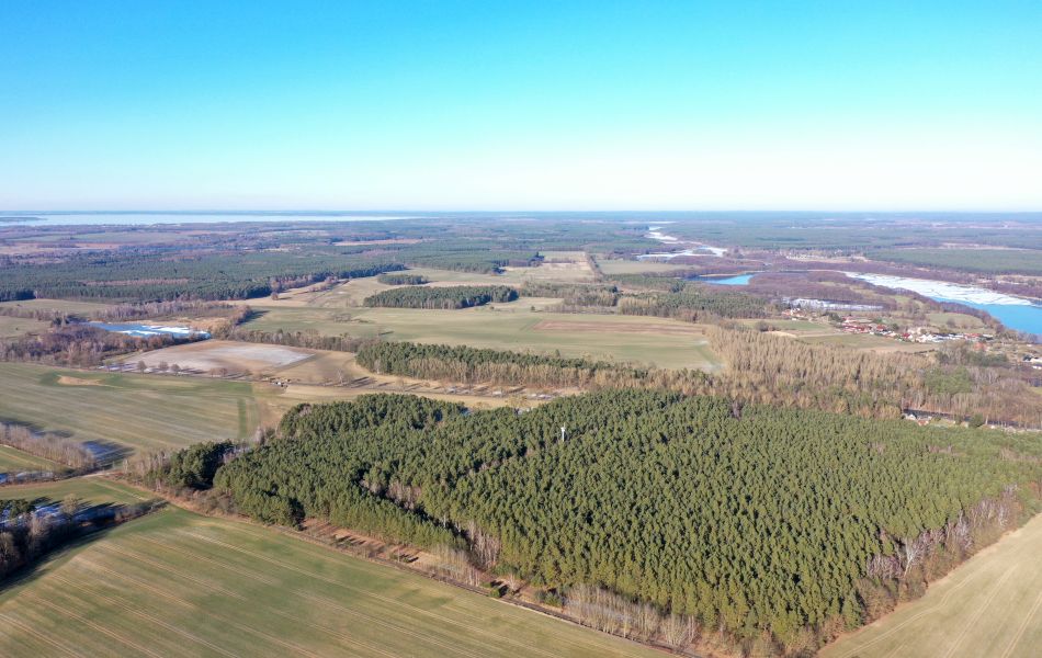 Blick über Felder und Wälder. Am rechten Bildrand sind ein See und Häuser der Stadt Mirow zu sehen. 