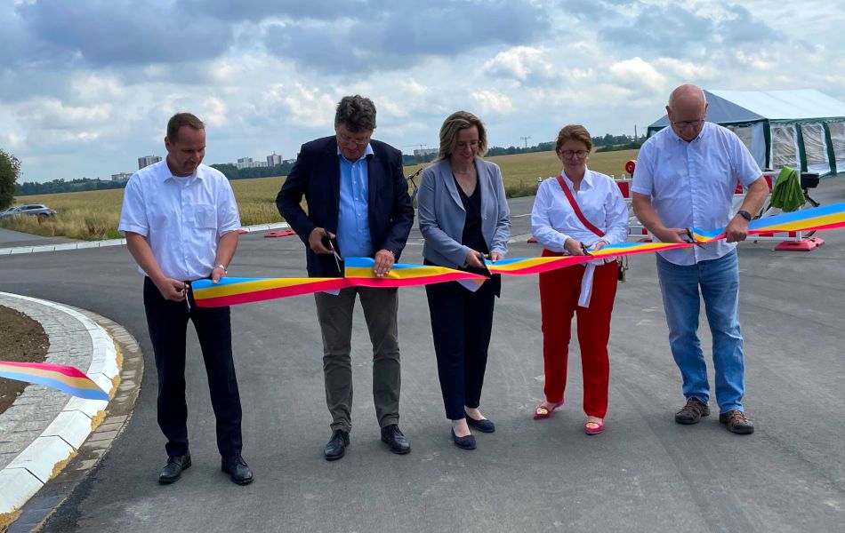 Drei Männer und zwei Frauen stehen auf der Straße eines Kreisverkehres und durchschneiden ein blau-gelb-rotes Band.