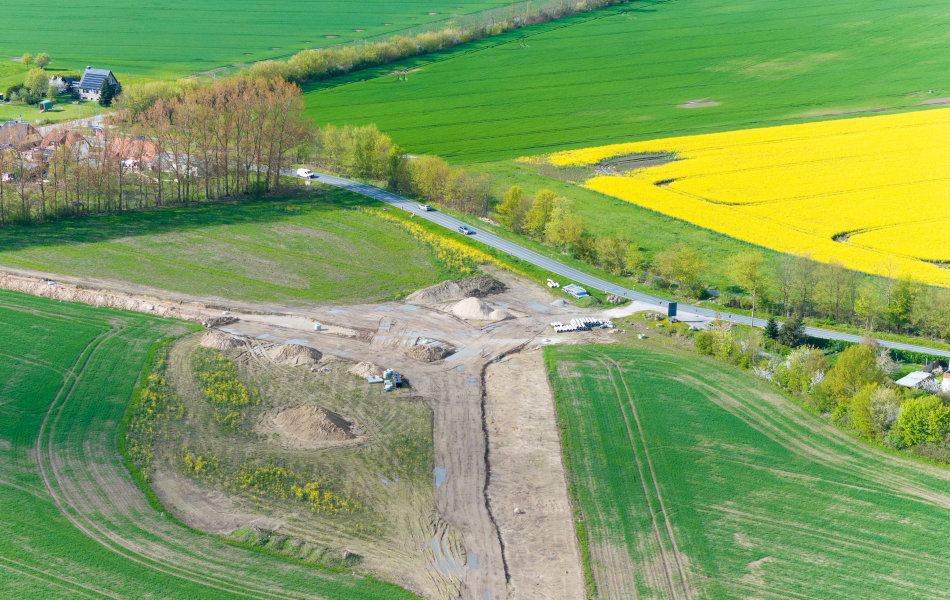 Auf einem Feld an einer Straße befinden sich mehrere Erdhaufen und zwei Wege, die aufeinandertreffen.