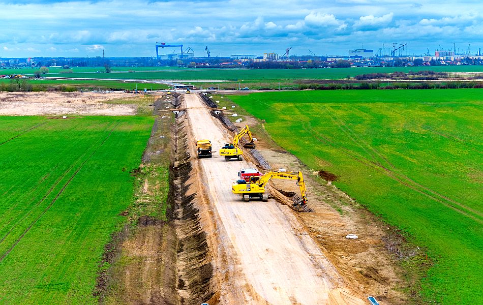 Zwei Bagger stehen auf einer Erdtrasse, die durch Felder hindurch führt, und baggern Gräben aus. Im Hintergrund ist die Stadt Rostock. © Pixelbox15 Zwei Bagger stehen auf einer Erdtrasse, die durch Felder hindurch führt, und baggern Gräben aus. Im Hintergrund ist die Stadt Rostock.