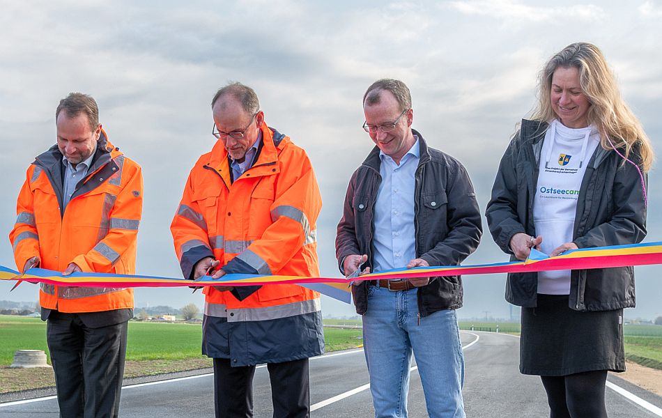 Drei Männer und eine Frau stehen auf einer neu gebauten Straße und lächeln. Sie haben symbolisch ein Band in den Farben Mecklenburg-Vorpommerns (blau, gelb und rot) durchgeschnitten und damit die neue Straße für den Verkehr freigegeben. © Pixelbox15 Drei Männer und eine Frau stehen auf einer neu gebauten Straße und lächeln. Sie haben symbolisch ein Band in den Farben Mecklenburg-Vorpommerns (blau, gelb und rot) durchgeschnitten und damit die neue Straße für den Verkehr freigegeben.