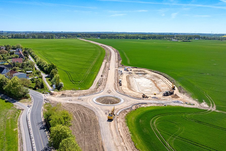 Auf einem Feld befindet sich ein kleiner ausgetrockneter See, der an einer Erdtrasse liegt. Die Erdtrasse führt zu einem Kreisverkehr und dann weiter parallel an einer Straße entlang. © Pixelbox15 Auf einem Feld befindet sich ein kleiner ausgetrockneter See, der an einer Erdtrasse liegt. Die Erdtrasse führt zu einem Kreisverkehr und dann weiter parallel an einer Straße entlang.