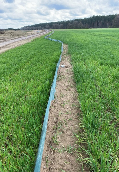 Auf einem Feld ist ein Zaun aus einer Plastikfolie errichtet worden, der an einer Trasse entlangführt.