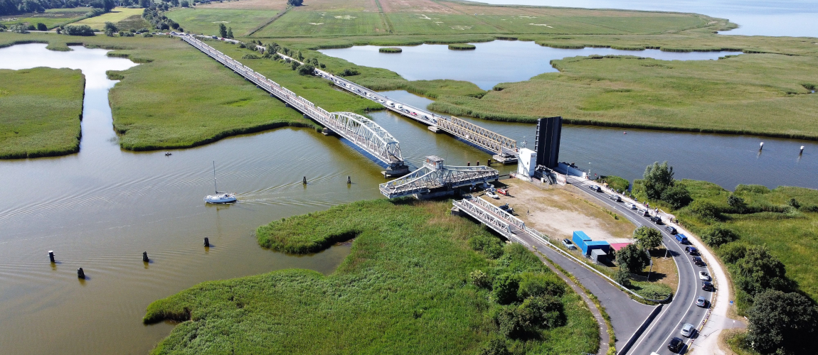 Blick von oben auf zwei parallel gelegene Brücken, die über einen Fluss, den Meiningenstrom, führen. Ein Abschnitt der rechten Brücke ist hochgeklappt und somit für die Schifffahrt geöffnet. Die Autos müssen davor auf der Straße warten. Bei der anderen Brücke ist ein Abschnitt quer zur Fahrbahn gedreht. Dadurch ist diese Brücke ebenfalls für Schifffahrt durchlässig.