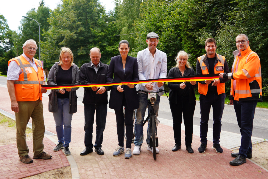 Mehrere Menschen schneiden gemeinsam ein Band durch. Sie feiern die Eröffnung eines neuen Radweges.
