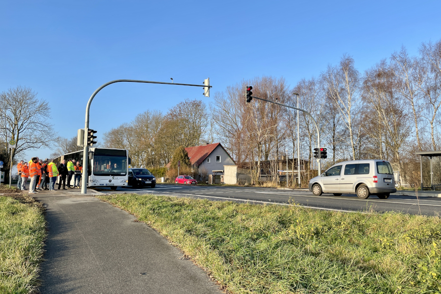 Kreuzung mit neuer Ampelanlage an der B 105; am Straßenrand stehen Personen in Warnwesten neben einem Bus, während Fahrzeuge an der roten Ampel warten.
