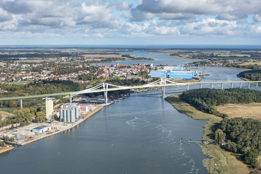 Visualisierung der künftigen Peenestrombrücke über den Peenestrom mit angrenzendem Stadtgebiet, Werftgelände und Wasserflächen.
