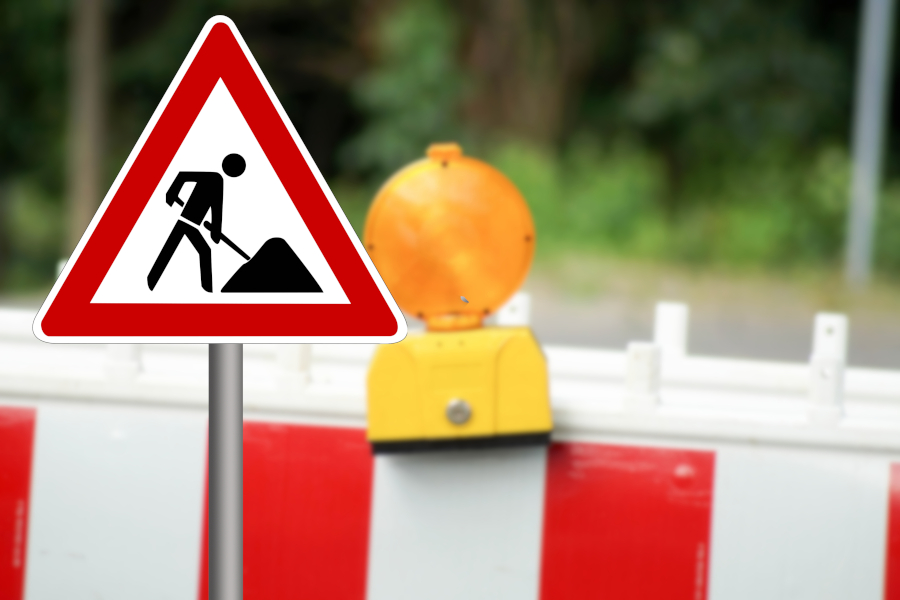 Verkehrszeichen &bdquo;Baustelle&ldquo; vor einer rot-weißen Absperrschranke mit gelber Warnleuchte
