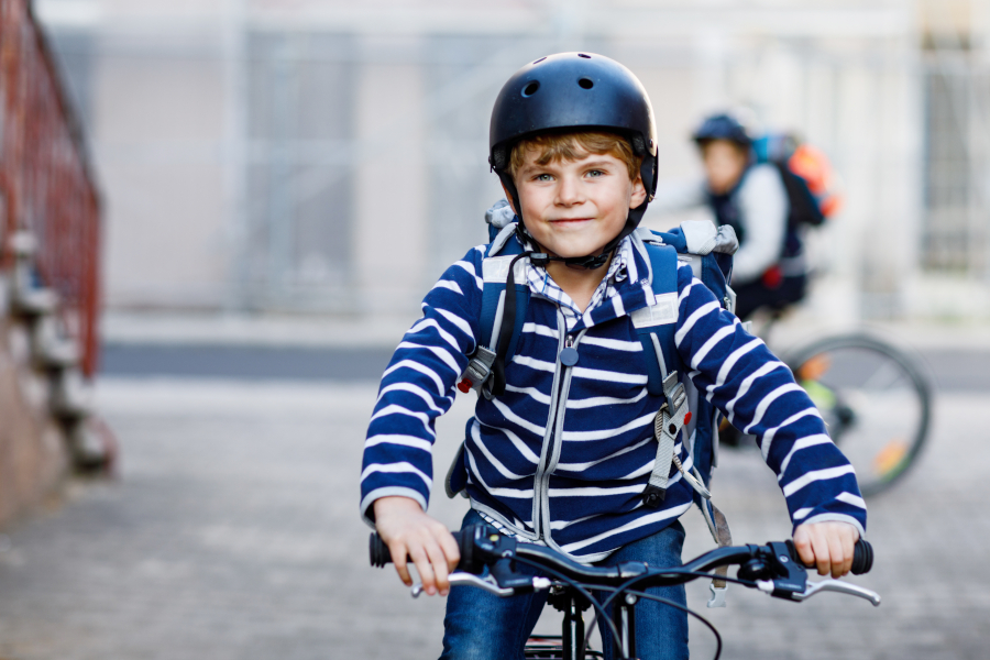 Zwei Schuljungen mit Schutzhelm fahren mit dem Fahrrad in der Stadt mit Rucksäcken.