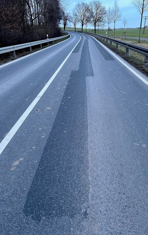 Auf einer Straße befinden sich mehrere, breitere, andersfarbige Asphalt-Streifen. 
