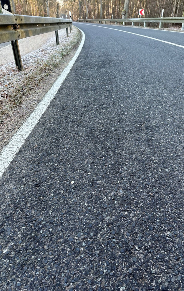 Der Asphalt einer Straße wirkt am Rand strak krisselig.