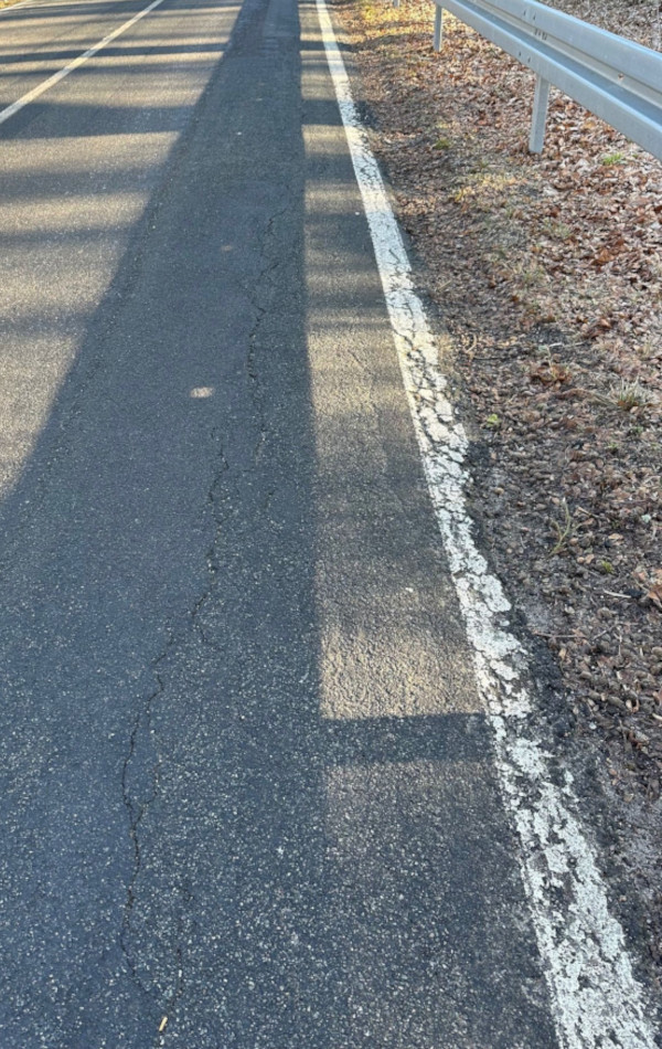 In einer Asphaltstraße führt ein langer Riss am rechten Rand der Fahrbahn entlang. Der betroffene Randbereich ist leicht abgesenkt.