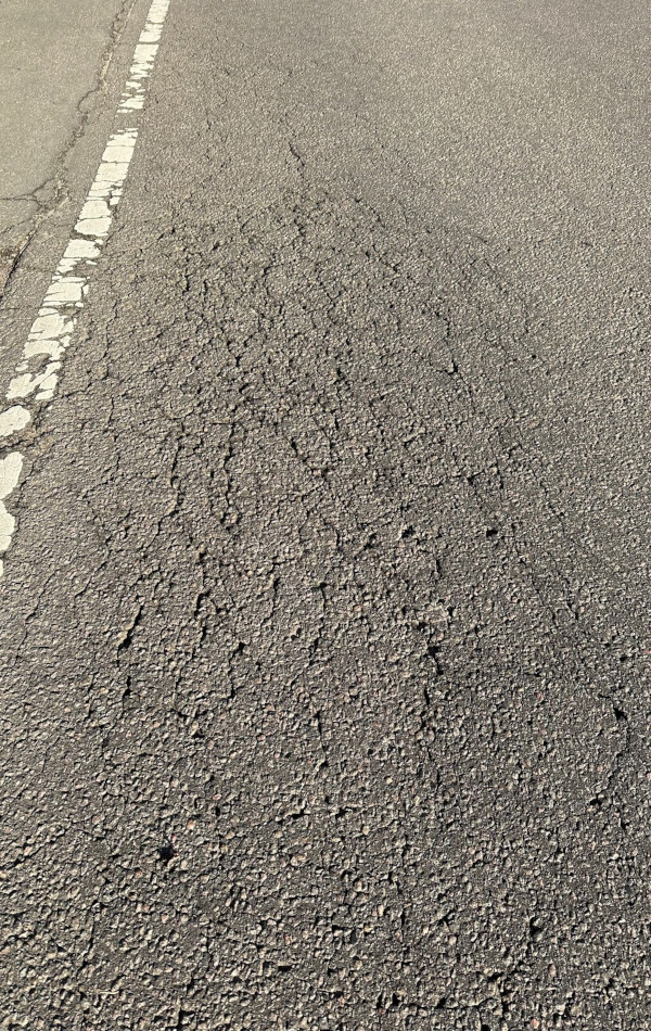 In einer Asphaltstraße breiten sich ganz viele kleine Risse wie ein Netz über die Fahrbahn aus.