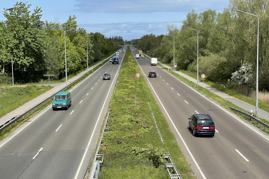 Autos fahren auf einer zweibahnigen Straße. Die beiden Fahrbahnen sind durch einen Grünstreifen in der Mitte getrennt.
