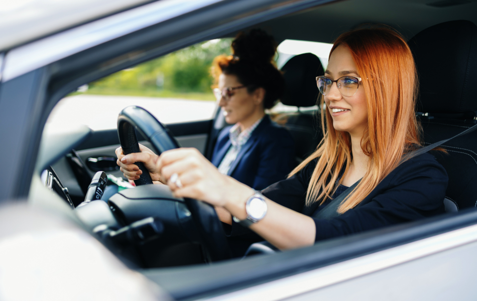 Eine junge rothaarige Frau hat mit ihrer Lehrerin Fahrschulunterricht.