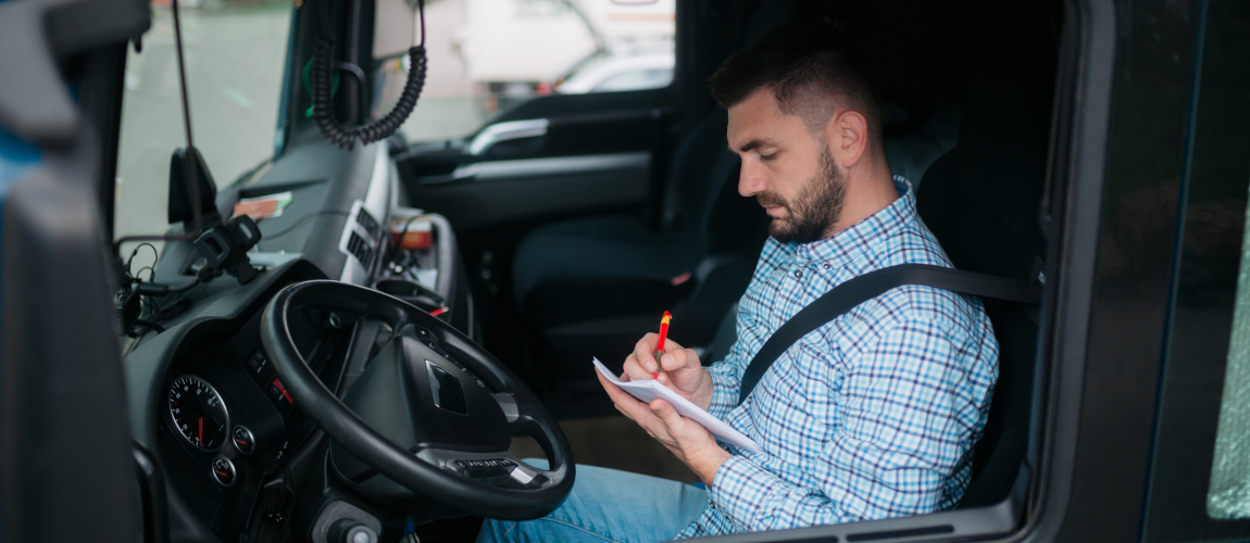 Seitenansicht eines LKW-Fahrers, der in einer Kabine in seinem LKW sitzt, einige Notizen aufschreibt und sich auf seine Reise vorbereitet. © iStock.com/Brothers91 Seitenansicht eines LKW-Fahrers, der in einer Kabine in seinem LKW sitzt, einige Notizen aufschreibt und sich auf seine Reise vorbereitet.