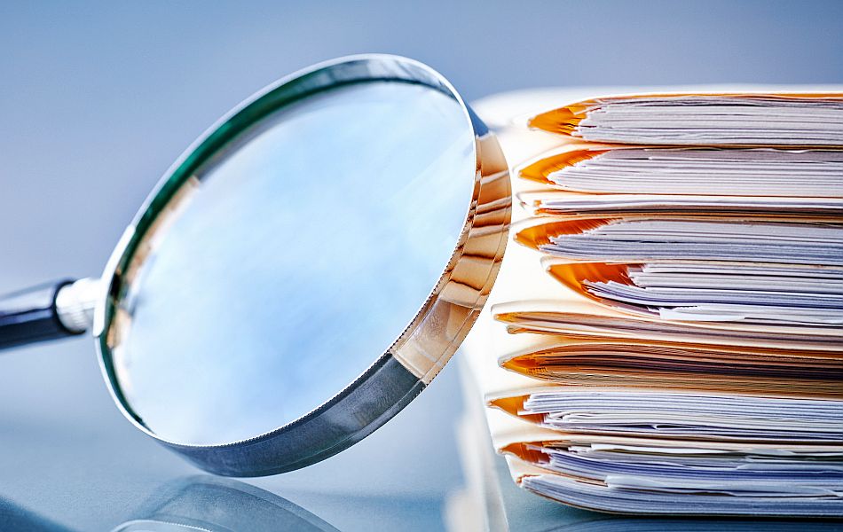 Vergrößerungsglas neben einem Stapel Akten und Dokumente auf einer glatten Oberfläche, sachliche Nahaufnahme.